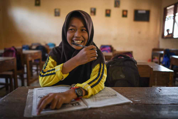 Girl wearing a hijab sitting at a schooldesk.