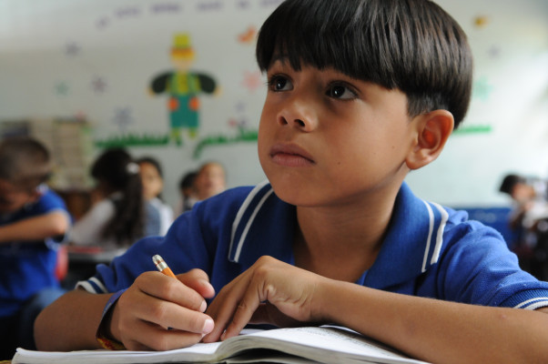 Close-up of child taking notes in classroom.