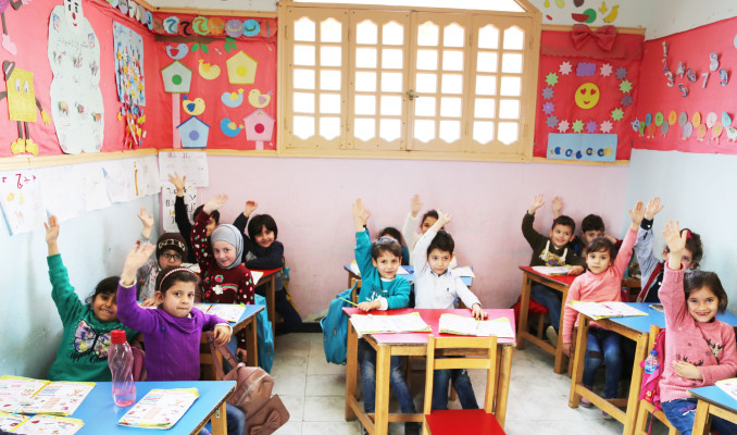 Primary school children at their desks raising their hands