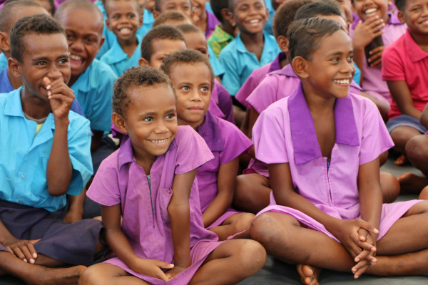 Boys in school uniform sitting crosslegged and smiling