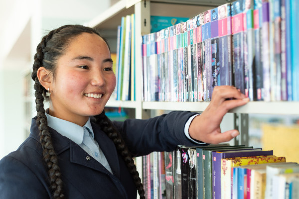 A teenage girl browses a library shelf.