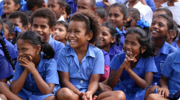 Students in blue uniforms smiling and watching something out of frame.