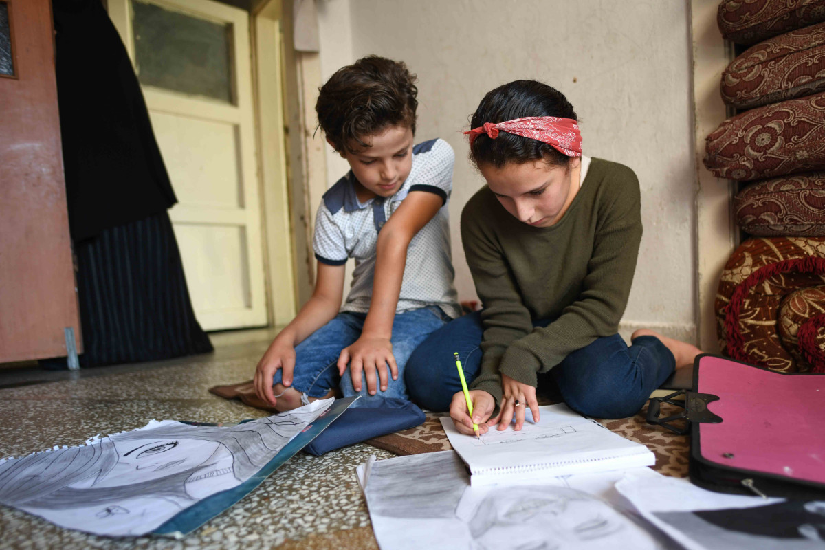 Two children sitting on ground looking at a notepad.