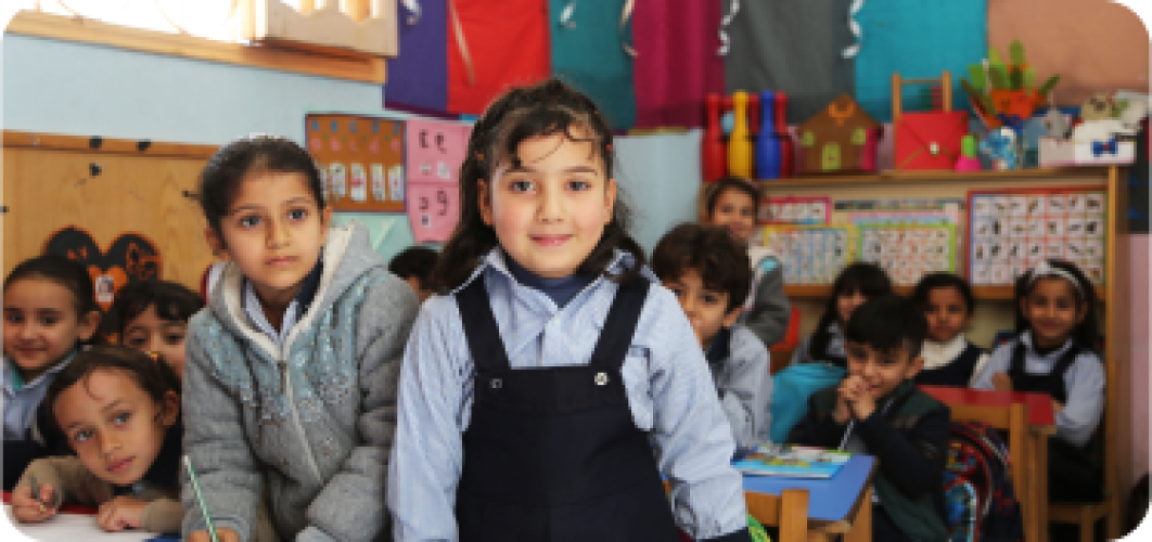 Girl smiling at camera with classroom filled with students behind her