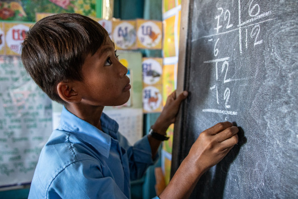 Veha (11) working out a math problem at a blackboard at his floating school on Tonle Sap Lake, Cambodia